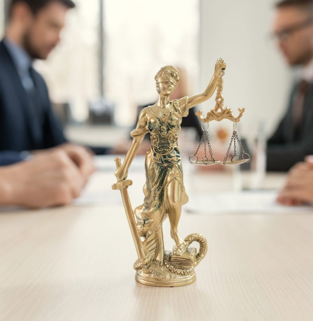 Figure of justice in the office Close-up of figure of justice standing on the table with group of lawyers sitting at meeting in the background